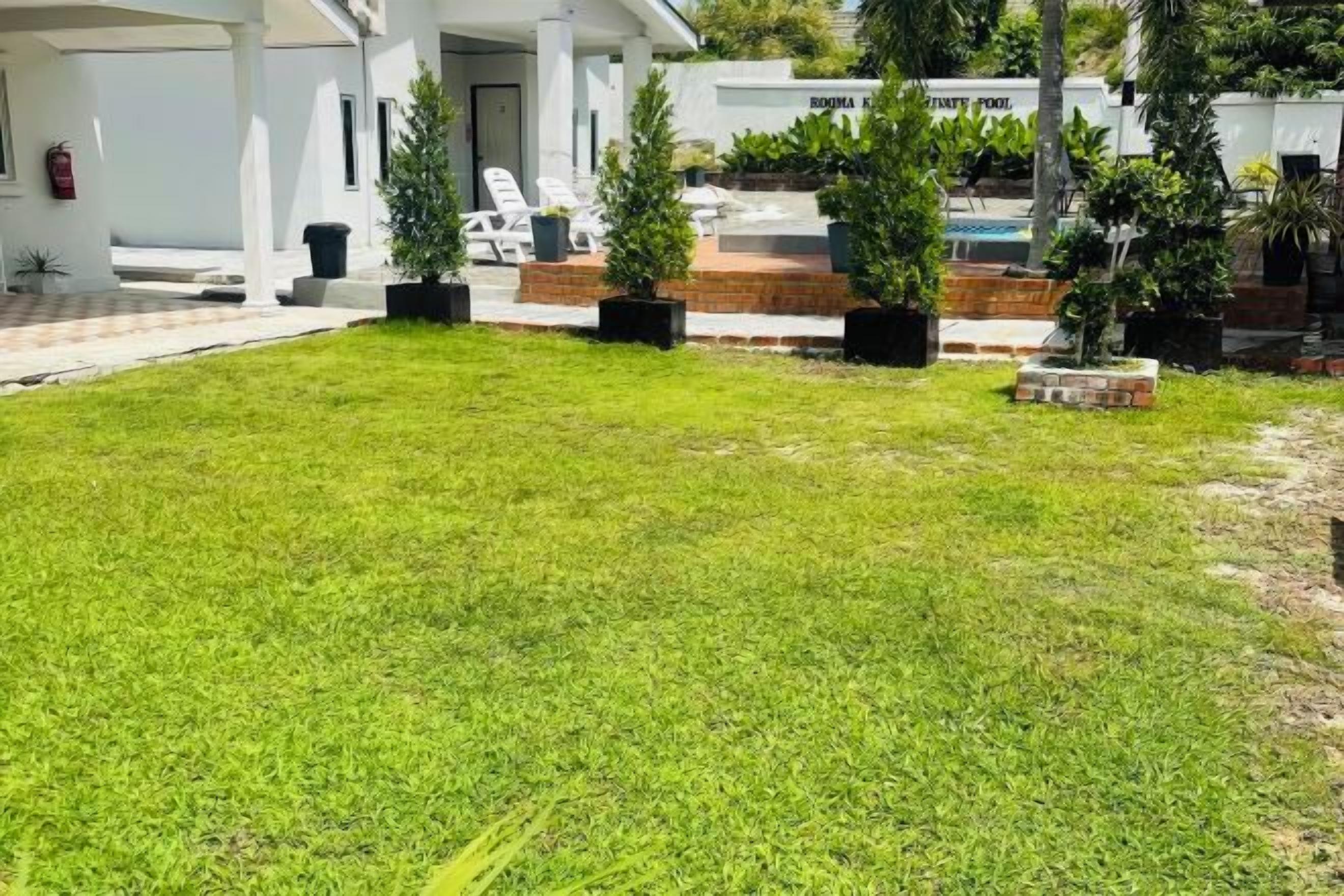 A well-maintained lawn with potted plants, a pool area, and a white building with a sign that reads "Infinity Pool".