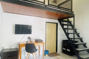 Una habitación con escritorio, silla, televisor y una escalera negra.
