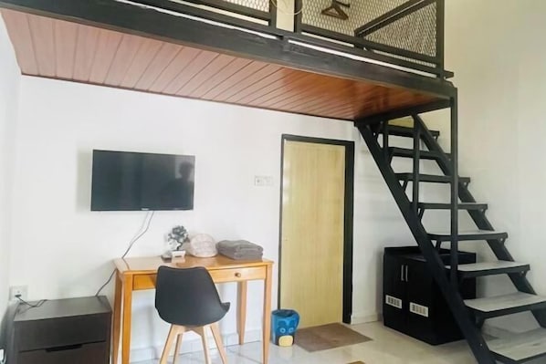 A room with a desk, chair, TV, and a black staircase.