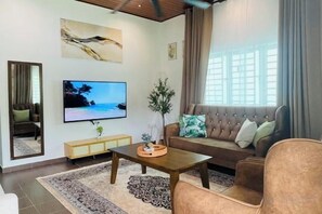 Un salon avec un canapé, une table basse, un téléviseur et une fenêtre avec des rideaux.