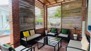 A sunlit patio area with outdoor seating, a pool, and a view of the pool area. - Rooma Kichi Private Pool (Langkawi)