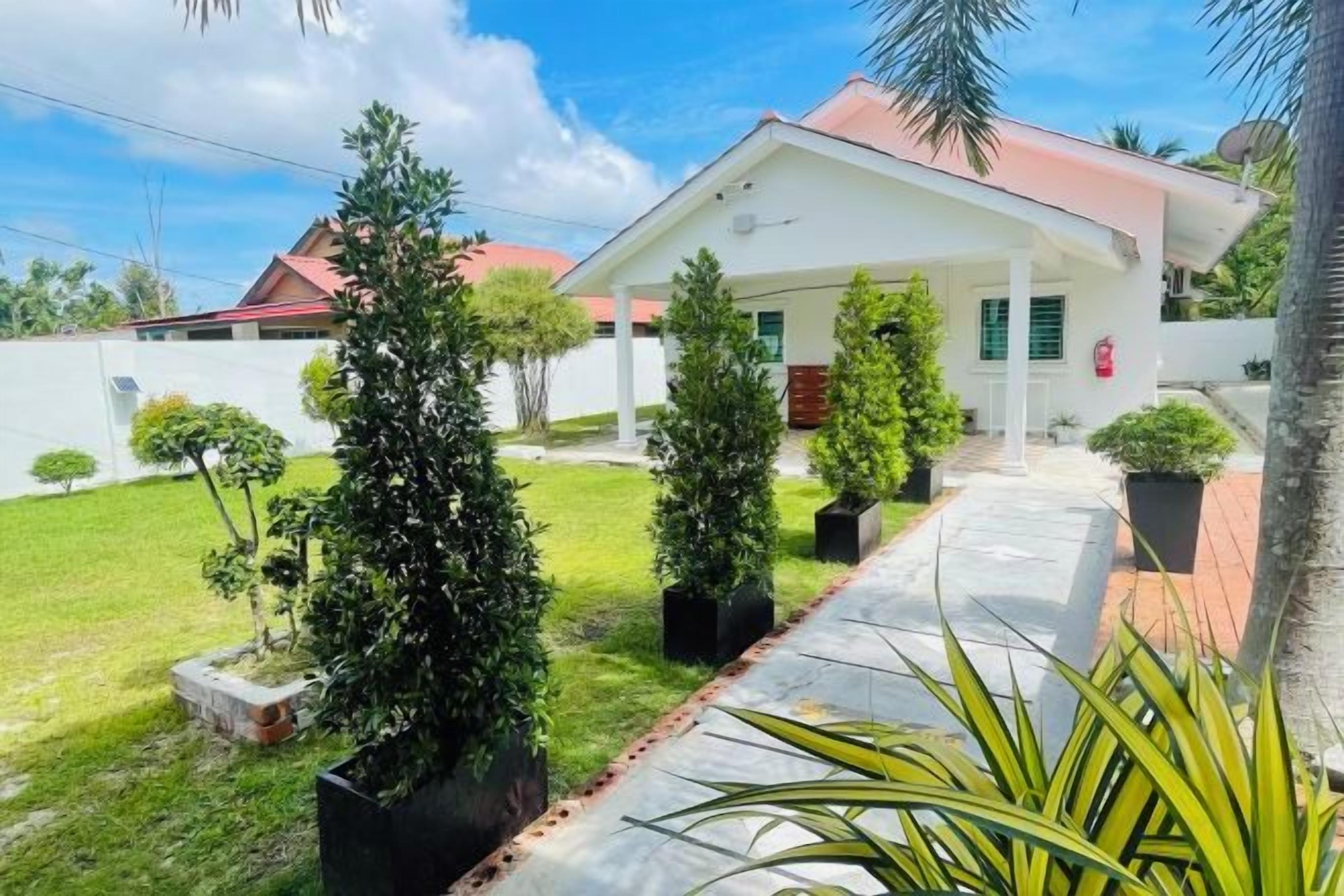A white building with a red roof, surrounded by a well-maintained lawn and potted plants.