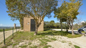 Een landelijk gebouw met één deur, omgeven door bomen en een omheind gebied.