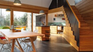 A modern kitchen with wooden cabinetry, a dining area with a table and chairs, and a staircase with wooden steps. - A contemporary Welsh Eco house, set in an acre of land nestled on the Preseli Hills above the sea (Newport)
