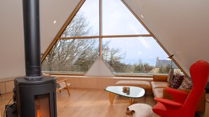 A cozy living room with a modern stove, a glass coffee table, a red chair, and a sofa with patterned cushions. - A contemporary Welsh Eco house, set in an acre of land nestled on the Preseli Hills above the sea (Newport)