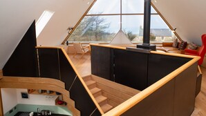 A modern loft-style room with a sloped ceiling, a built-in fireplace, and a view of the outdoors. - A contemporary Welsh Eco house, set in an acre of land nestled on the Preseli Hills above the sea (Newport)