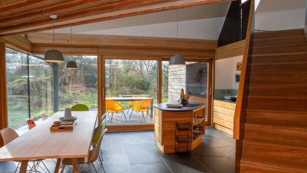 A modern kitchen with wooden cabinetry, a central island, and a dining area with a large table and chairs. - A contemporary Welsh Eco house, set in an acre of land nestled on the Preseli Hills above the sea (Newport)