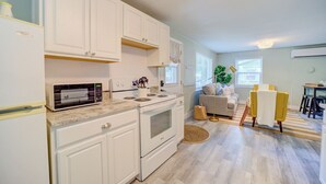 A modern kitchen with white cabinets, a microwave, stove, and oven. There is a dining area with a sofa and a yellow chair. - Scenic Drive Resort - Cabin #1 (Muskegon)