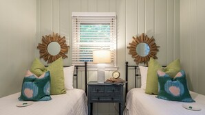 Une chambre avec deux lits, une table de chevet, une lampe et des miroirs décoratifs.