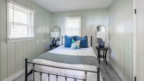 A bedroom with a bed, two bedside tables, two lamps, and two windows with blinds. - Scenic Drive Resort - Cabin #7 (Muskegon)