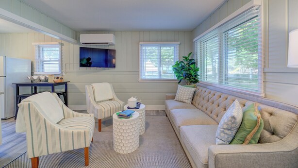 A cozy living room with a striped armchair, a round coffee table, and a beige sofa with patterned cushions. - Scenic Drive Resort - Cabin #7 (Muskegon)
