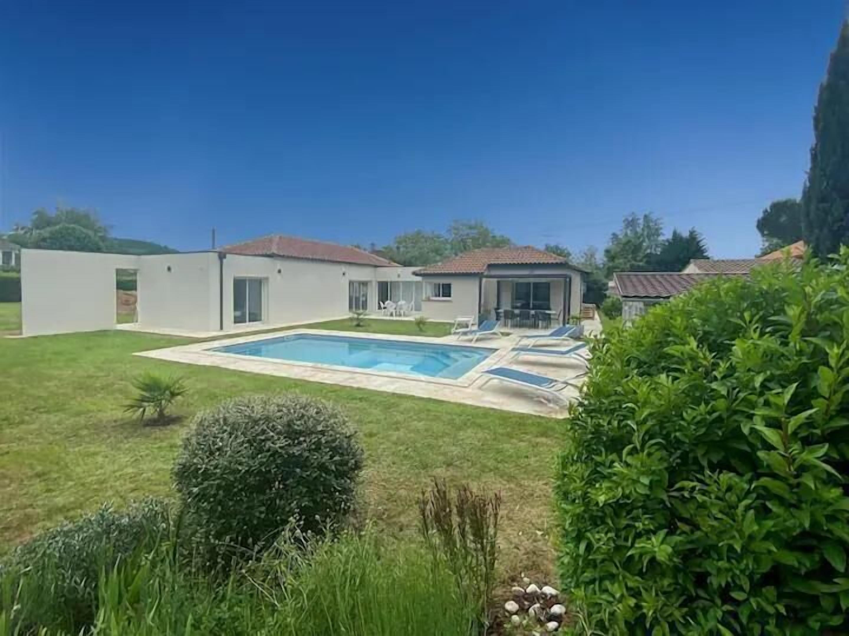 Une maison moderne dotée d’une piscine, d’un patio avec des chaises longues et d’un jardin bien entretenu.