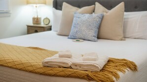 Een net opgemaakt bed met een gevouwen witte handdoek, een bruine plaid en een kussen met een patroon.