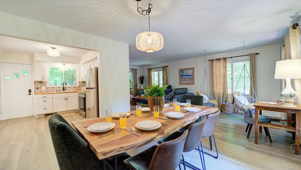 Een ruime keuken met moderne apparatuur, een eetgedeelte met een houten tafel gedekt voor vier personen, en een gezellige zithoek met een bank en een hangstoel.