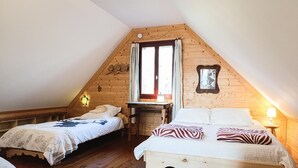 Ein gemütliches Schlafzimmer im Dachgeschoss mit zwei Betten, Holzwänden, einer geneigten Decke und einem kleinen Tisch.