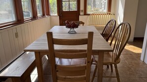 Un comedor con mesa y sillas de madera, un banco y una ventana con vista a árboles.