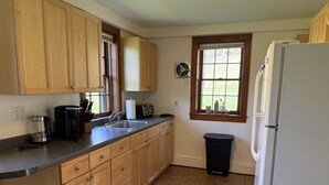 Una cocina con armarios de madera, un lavamanos, un refrigerador y una ventana con persianas.
