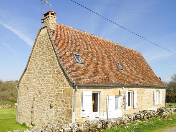 A stone farmhouse with a steeply pitched roof and a chimney.