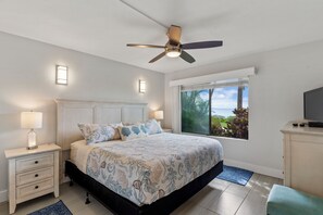 Ein Schlafzimmer mit Bett, Nachttisch, Lampe, Deckenventilator, Fenster und Fernseher.