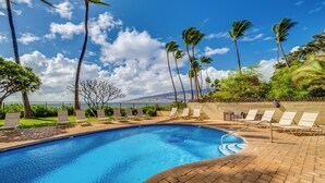 A swimming pool with lounge chairs, palm trees, and a clear sky.