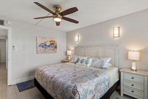 A bedroom with a bed, nightstands, a ceiling fan, and wall-mounted lights.