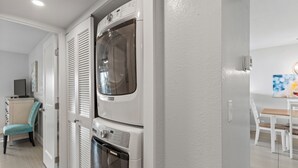 Une buanderie équipée de machines à laver et de sèche-linge superposés, d’une chaise et d’une table avec des chaises dans l’espace repas adjacent.