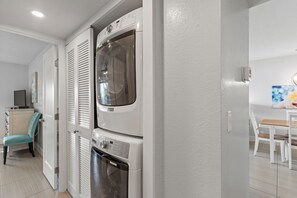 A laundry room with stacked washers and dryers, a chair, and a table with chairs in the adjacent dining area.