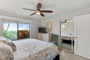 Ein Schlafzimmer mit Bett, Fernseher, Deckenventilator, Fenster mit Blick und einer Tür.