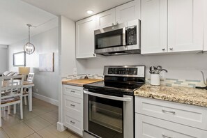 A modern kitchen with white cabinetry, a built-in microwave, a stove, and a dining area with a table and chairs.