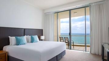 A hotel room with a large bed, a nightstand, a desk, and a view of the ocean.