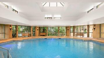Una amplia piscina interior con paredes de vidrio transparente, bancos y un techo con tragaluces.