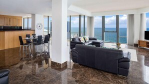 A modern living room with a large black sofa, a dining area with a table and chairs, and a kitchen with wooden cabinets. - Mantra Sun City Surfers Paradise (Gold Coast)