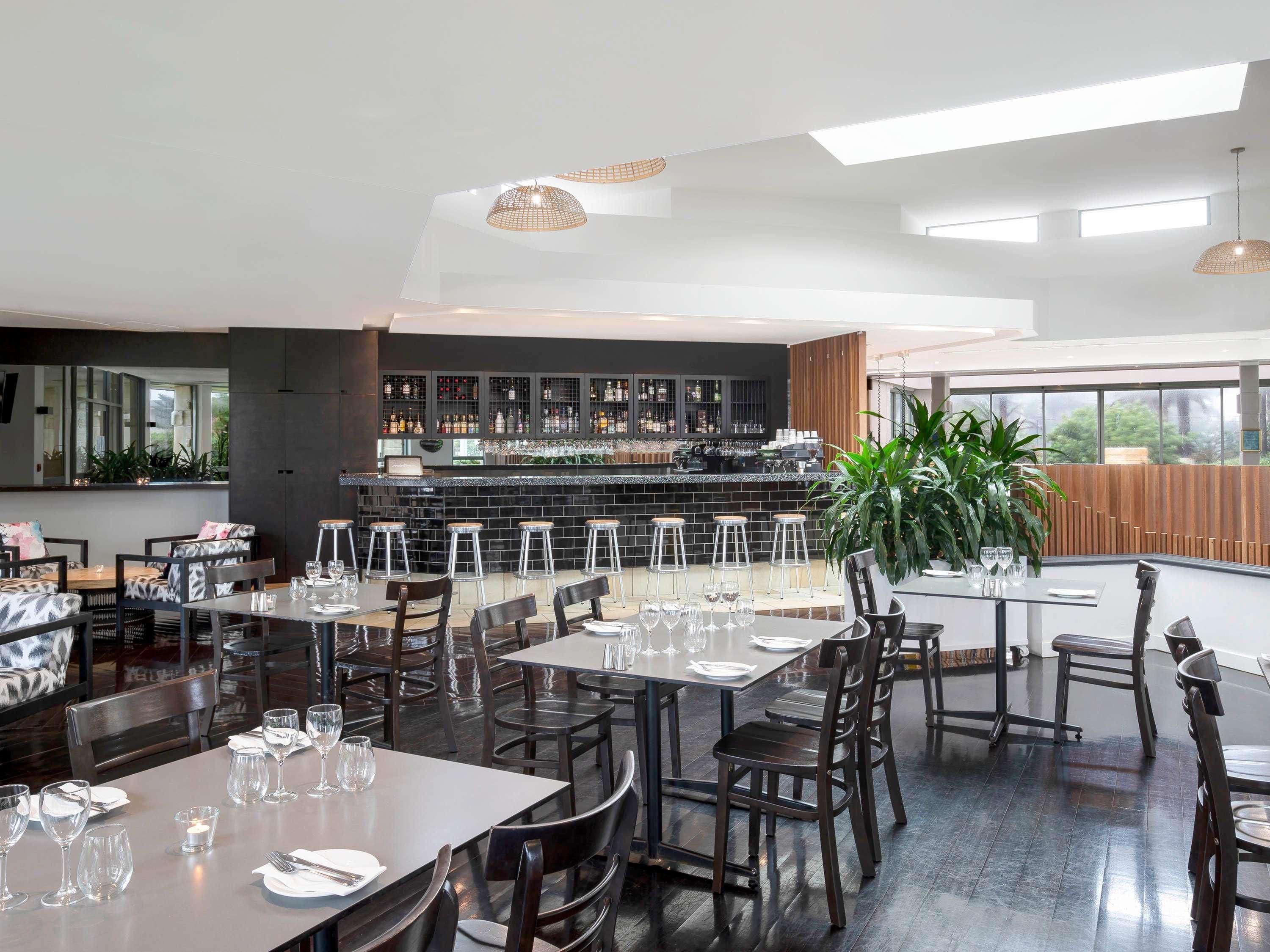 Um restaurante moderno com área de bar, várias mesas e cadeiras.
