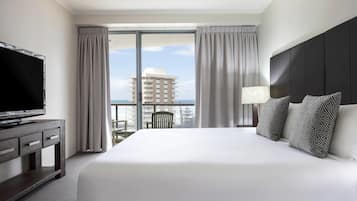 A hotel room with a large bed, a TV on a wooden cabinet, a balcony with curtains, and a view of a building.