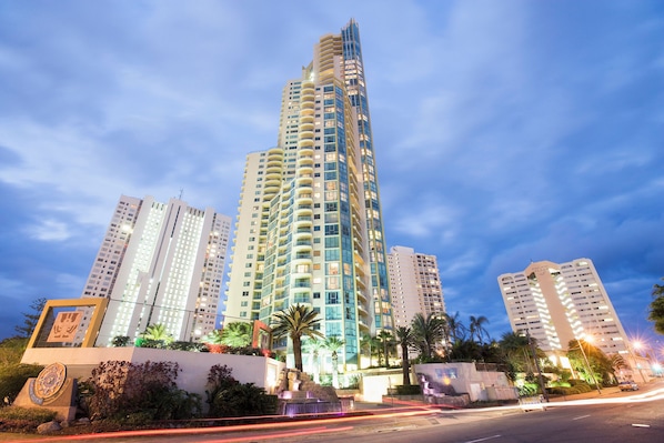 Un edificio alto con varios balcones, rodeado de palmeras y otra vegetación.