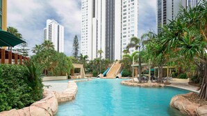 A swimming pool with a rock-lined edge, surrounded by palm trees and a small waterfall feature. - Mantra Sun City Surfers Paradise (Gold Coast)