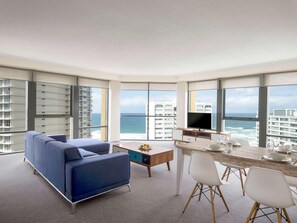 A modern hotel room with a large balcony, a sofa, a dining table with chairs, and a TV. - Mantra Sun City Surfers Paradise (Gold Coast)