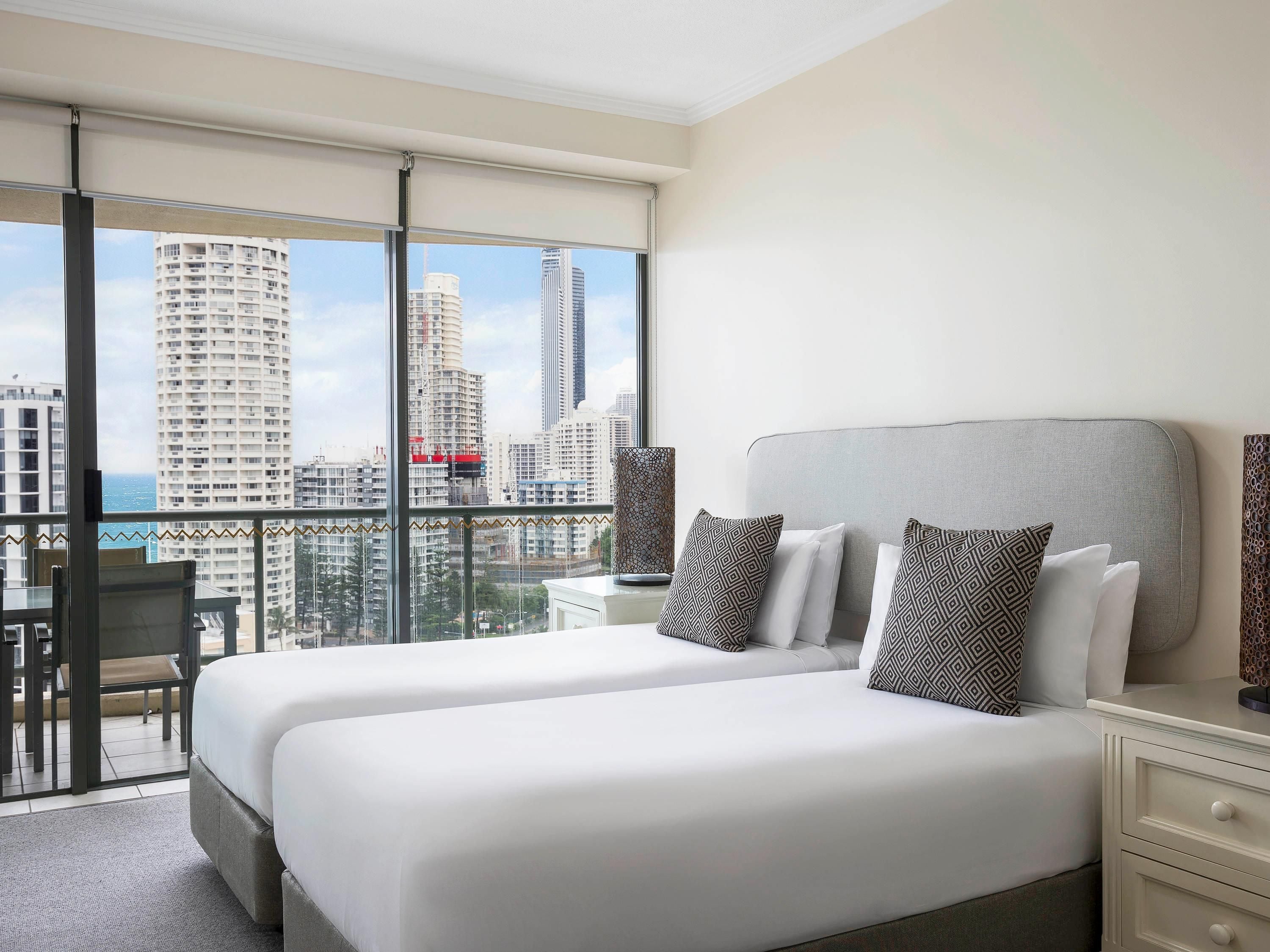 Habitación de hotel con dos camas, un balcón y vista a la ciudad, un escritorio y una silla.
