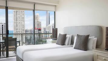 Habitación de hotel con dos camas, un balcón y vista a la ciudad, un escritorio y una silla.