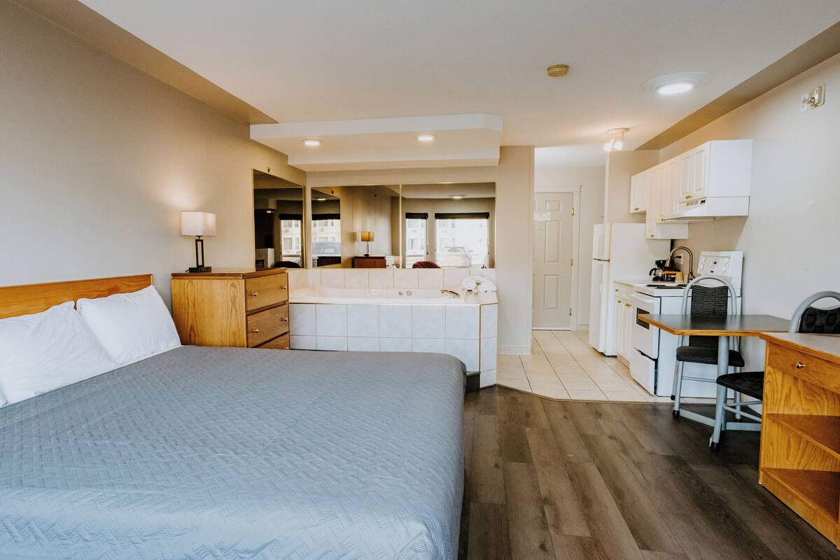 A bedroom with a large bed, a desk, and a kitchenette.