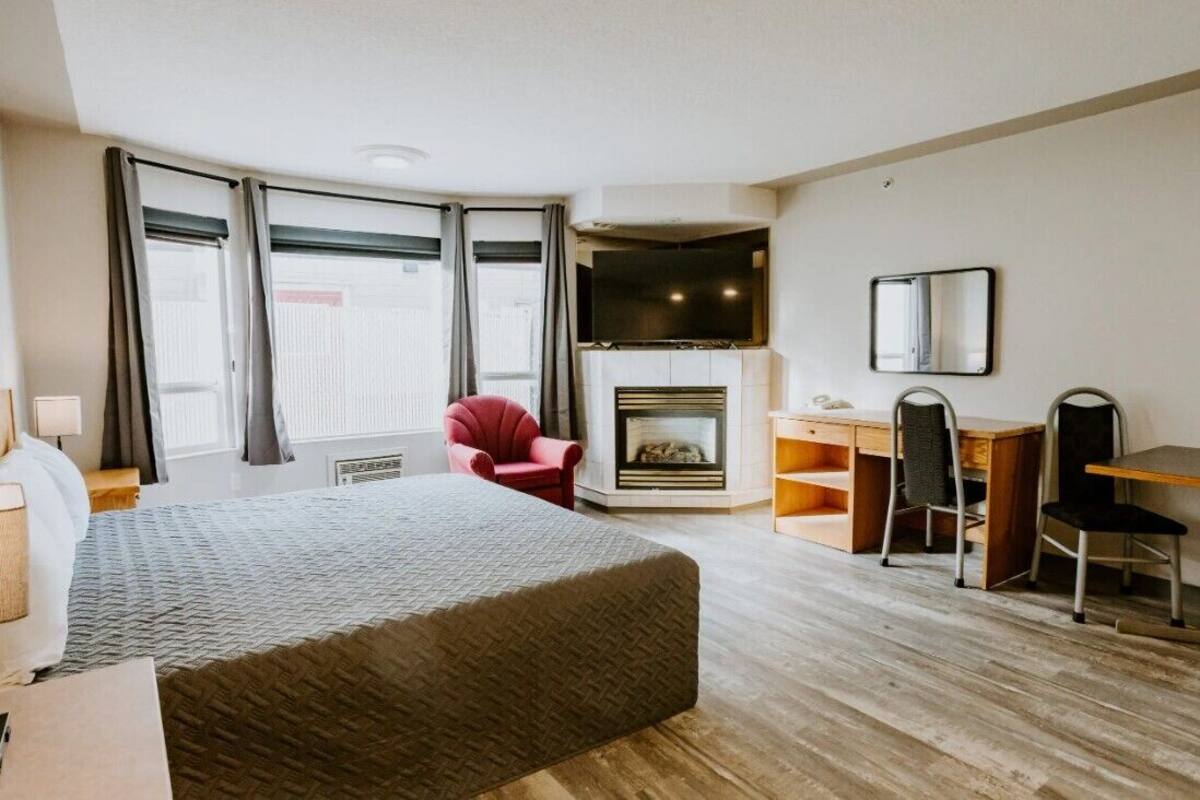 A hotel room with a bed, a desk, a chair, a fireplace, and large windows.
