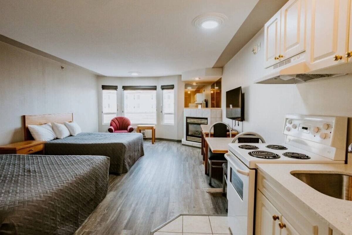 A compact hotel room with two beds, a kitchenette, a dining area, and a TV.