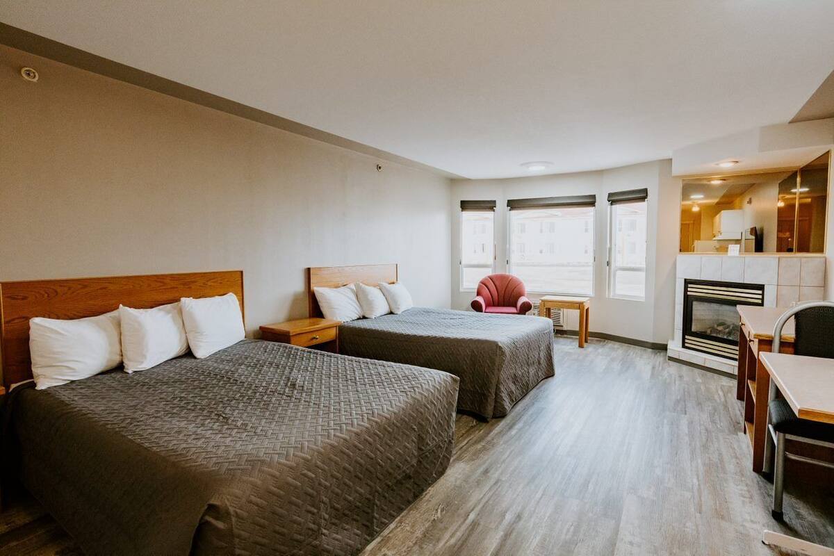 A hotel room with two beds, a small table, a chair, and a fireplace.