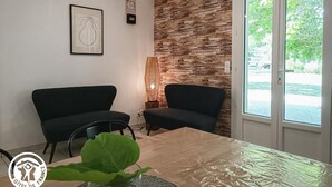 Et moderne værelse med to sorte sofaer, et spisebord og et stort vindue med udsigt til grønne omgivelser.