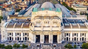 A large, historic building with a central dome and symmetrical facade, surrounded by modern structures.