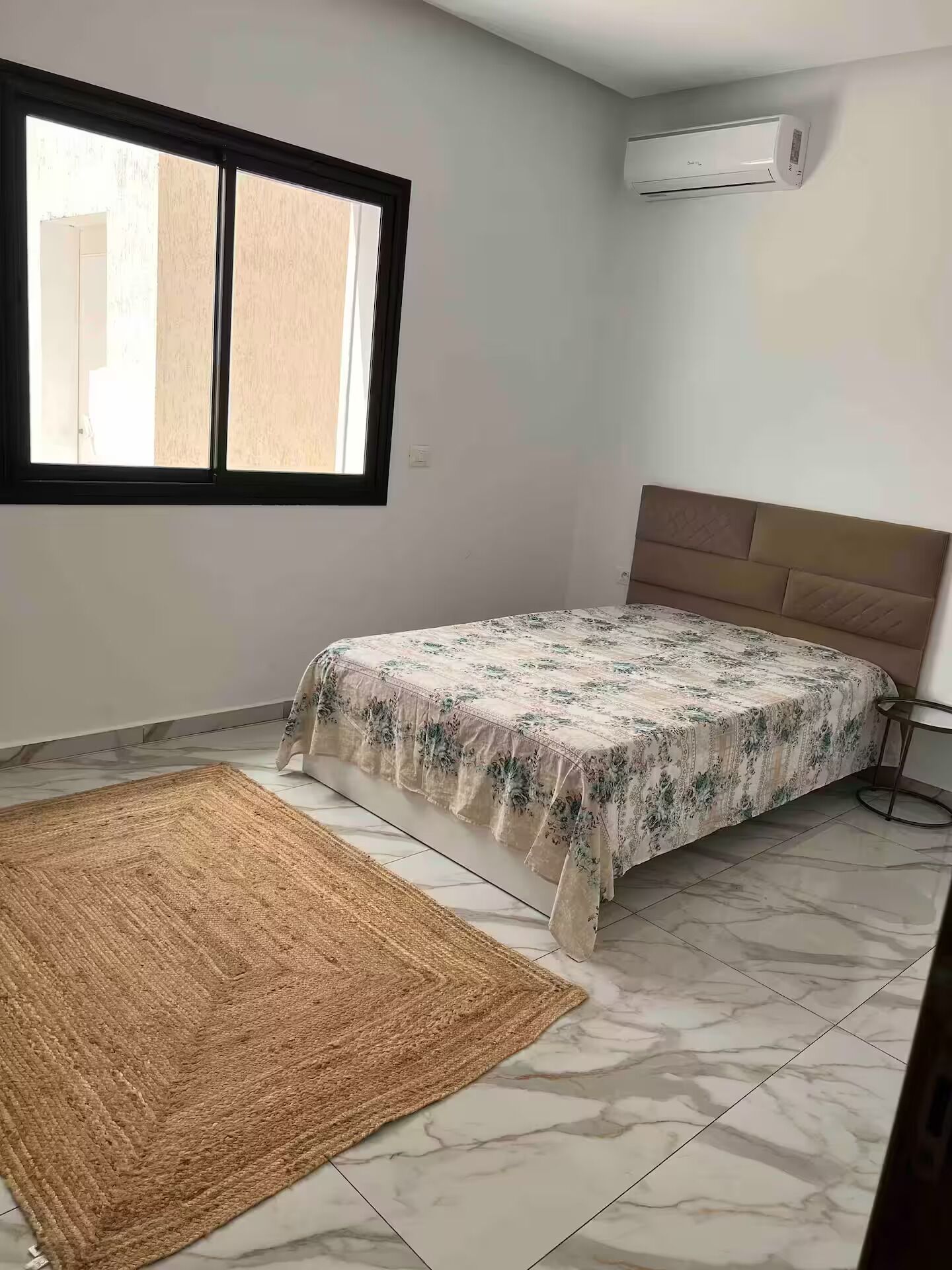 A bedroom with a bed, a window, an air conditioner, and a rug.