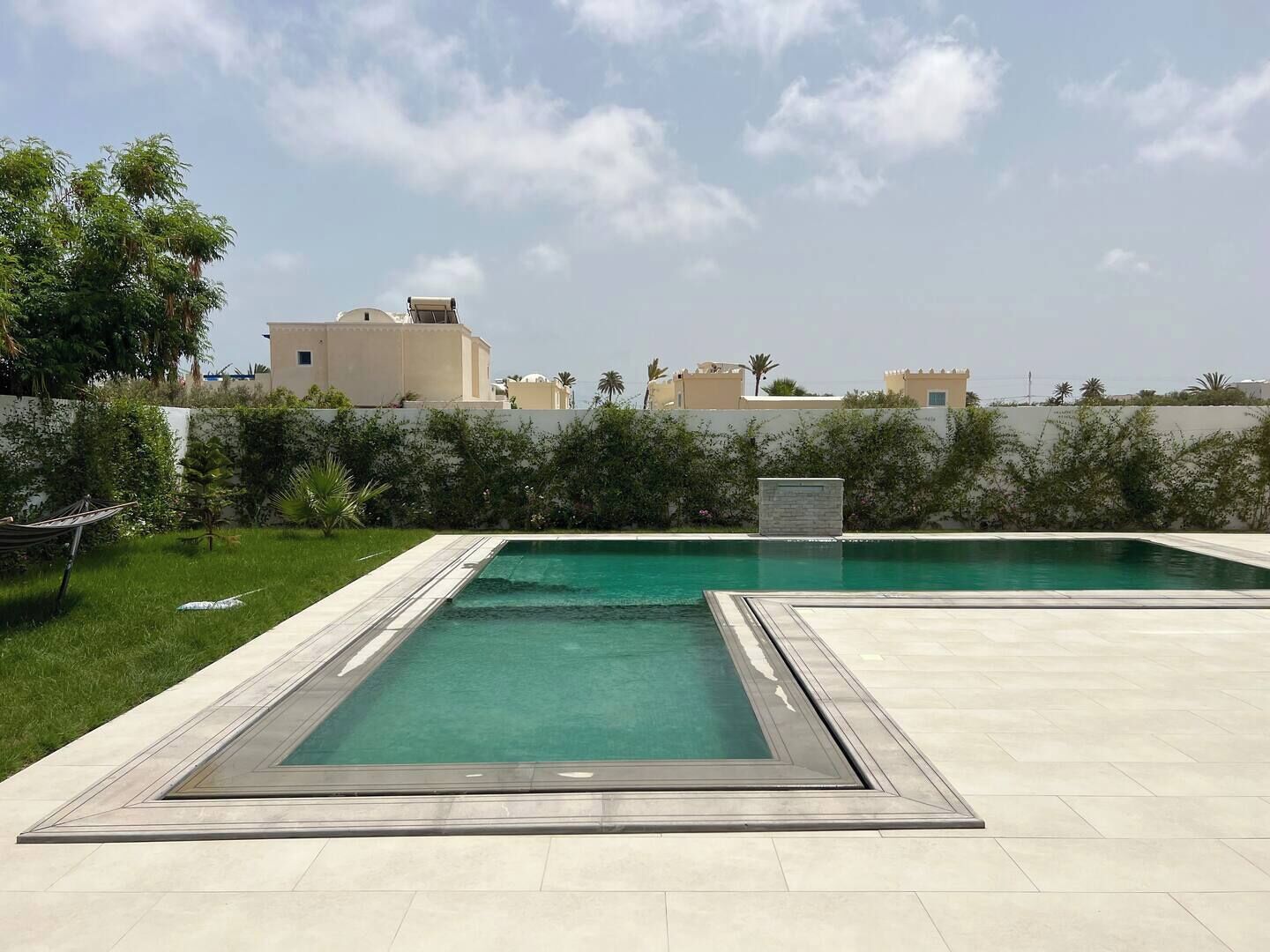 Ein rechteckiger Pool mit gefliestem Sonnendeck, umgeben von einer niedrigen Hecke und einer Rasenfläche.