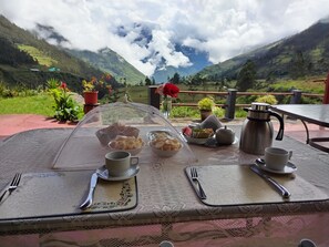 A table set with a teapot, cups, and a basket of cookies, overlooking a mountainous landscape. - Casa de Salcantay (San Pedro de Cachora)