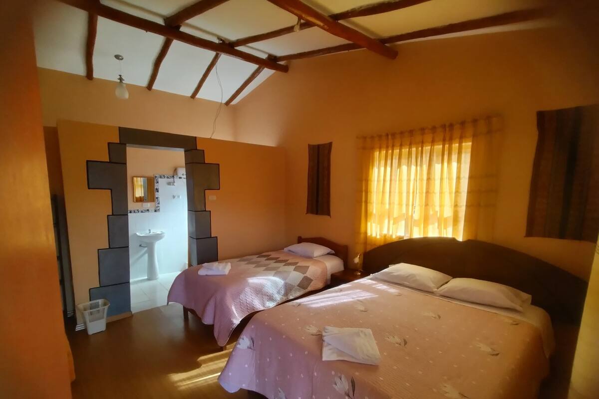 A room with two beds, a wooden ceiling, and a window with curtains.