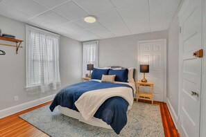 A bedroom with a bed, nightstands, a lamp, a window with curtains, and a door.